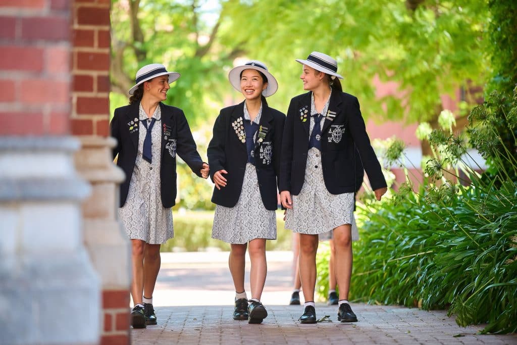 Schoolgirls in uniforms walking and laughing outside.