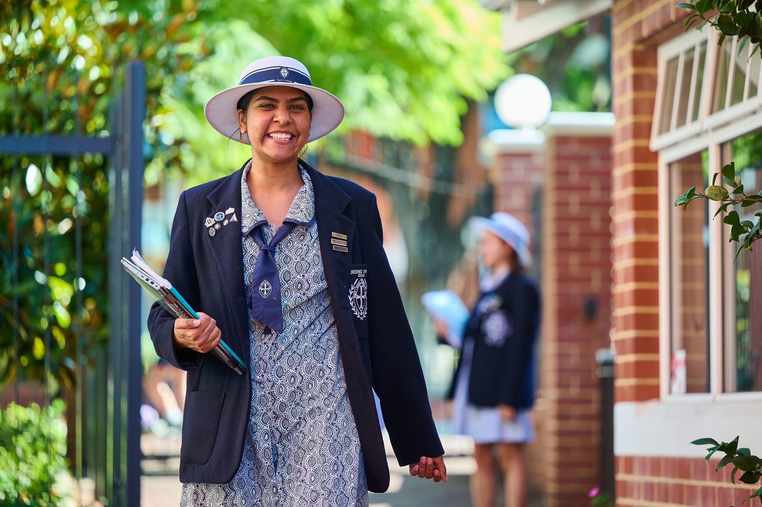 Schoolgirl in uniform smiling, holding textbooks.